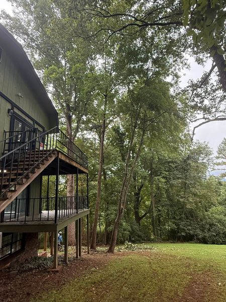 Green house with outdoor stairs and a grassy yard, trees in the background.