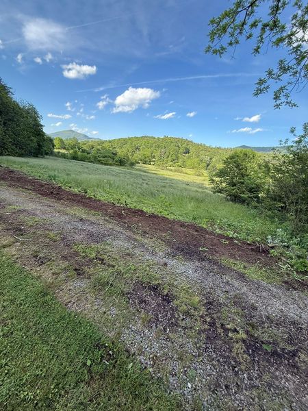 Green hillside with blue sky and scattered clouds, a dirt path in the foreground.