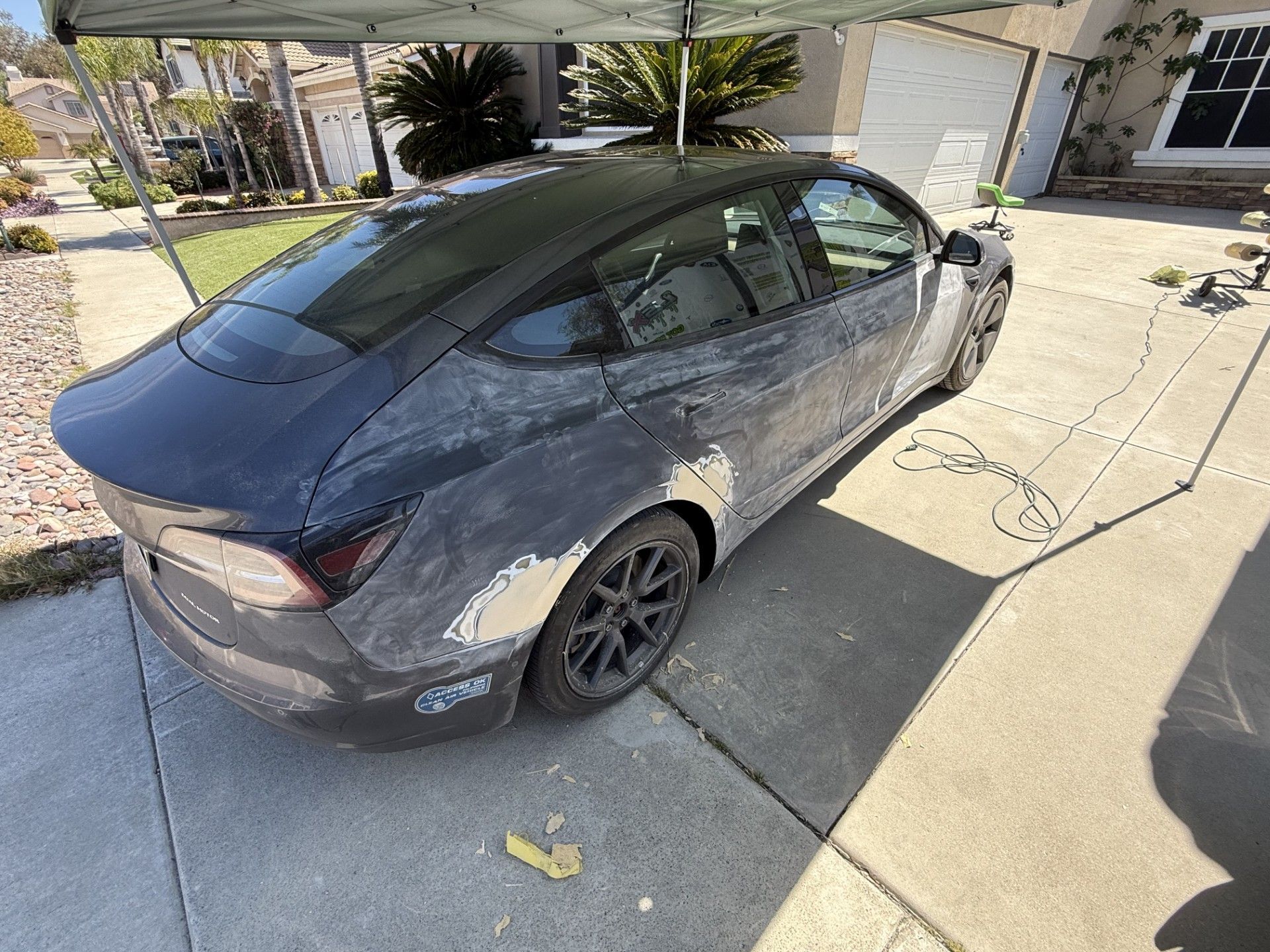 A tesla model 3 is parked in a driveway under a canopy.