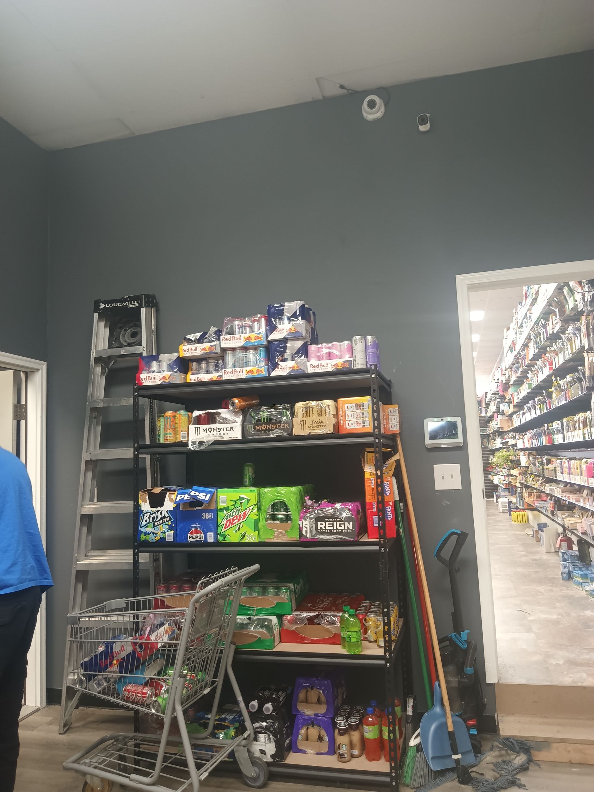 A tall, black metal retail shelf filled with packaged snacks sits against a grey wall next to an open doorway.