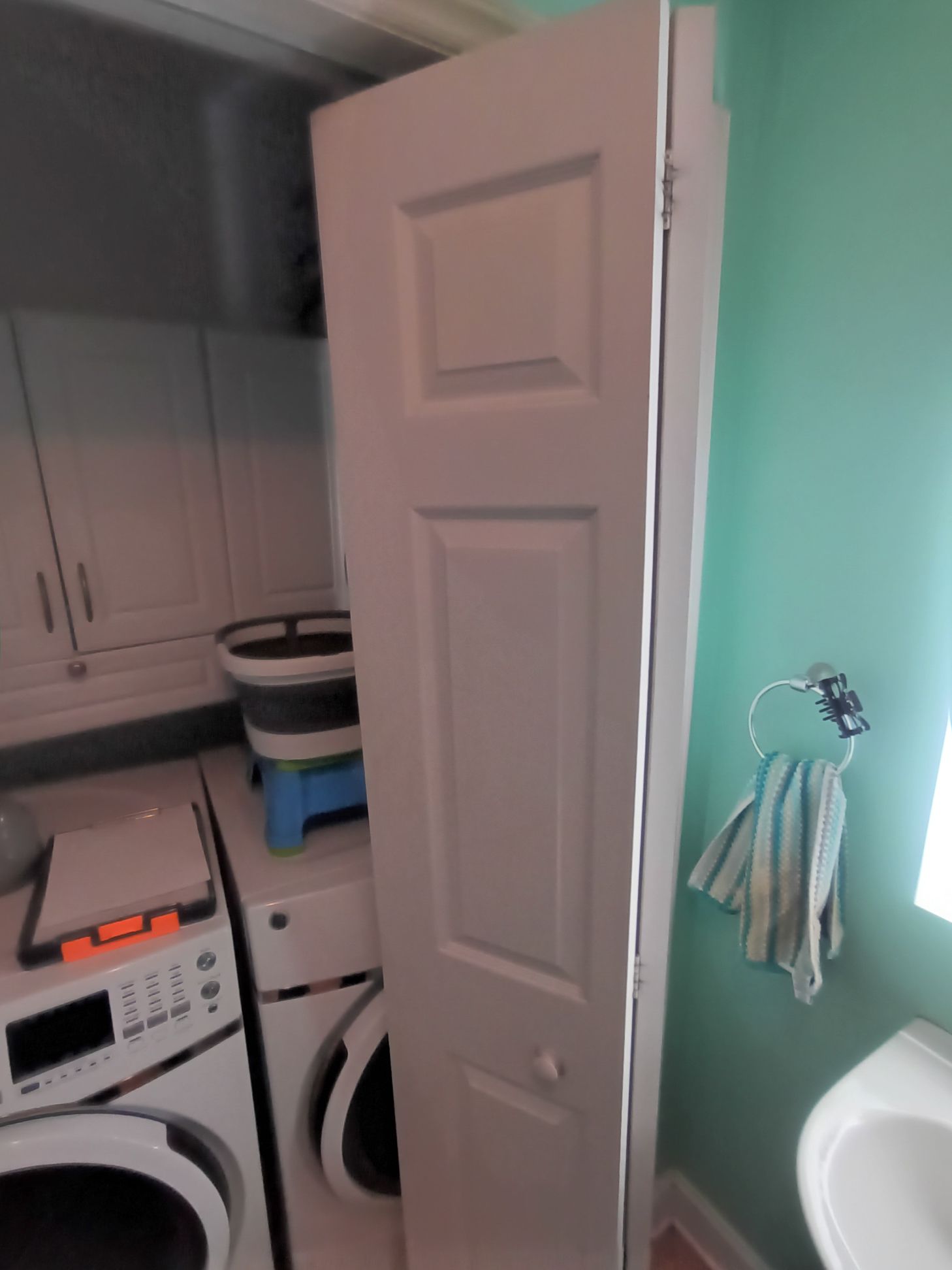 A bi-fold door stands closed in a laundry room next to a white washing machine and a mint green wall with a towel ring.