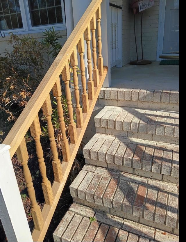 A wooden handrail with balusters runs alongside a set of light-colored brick outdoor steps leading to a house entrance.