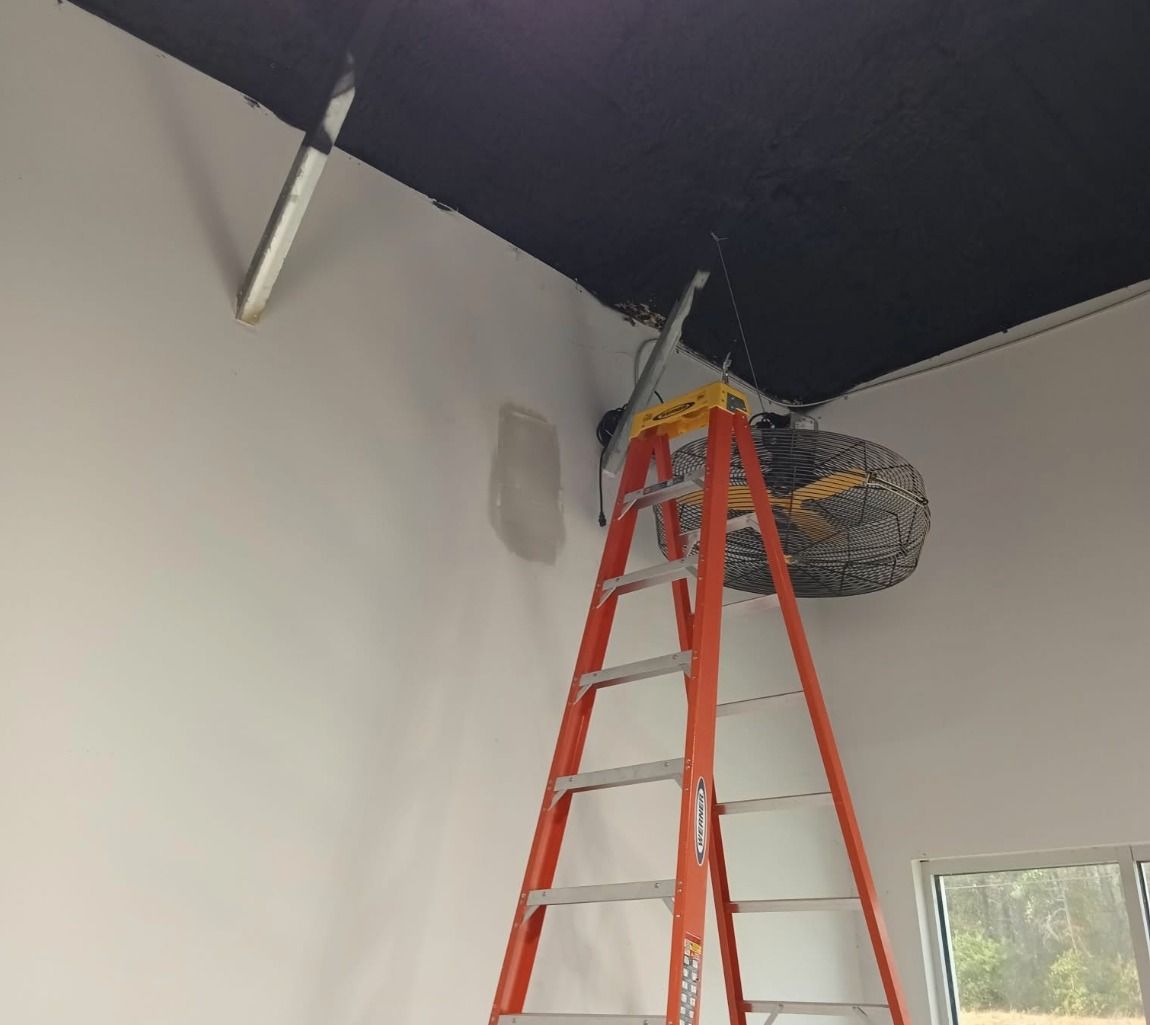 An orange ladder stands in a corner with a black ceiling and white walls, reaching toward an object mounted near the top.