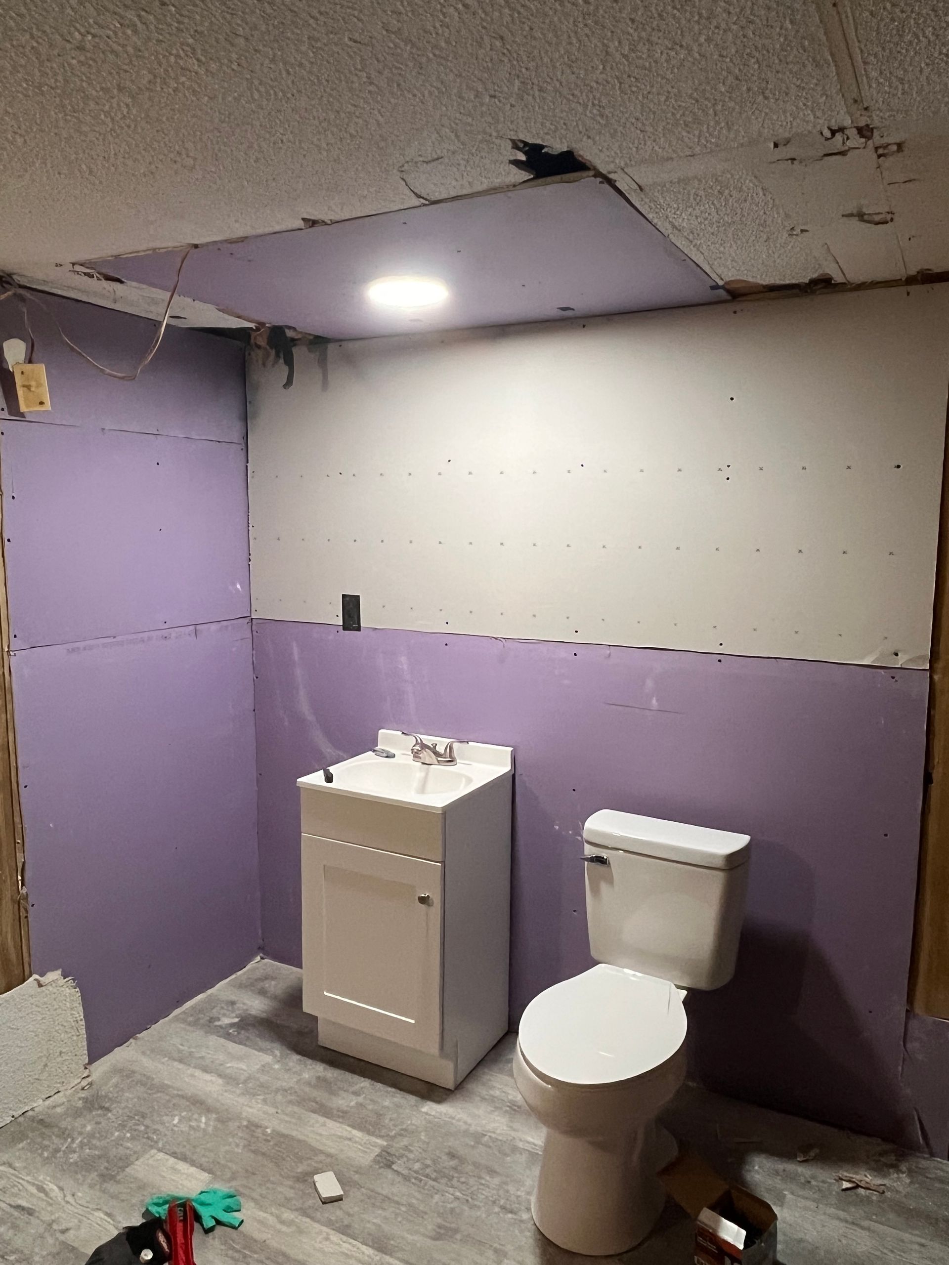 A partially renovated bathroom with purple drywall, a white vanity sink, and a toilet on grey wood-look flooring.