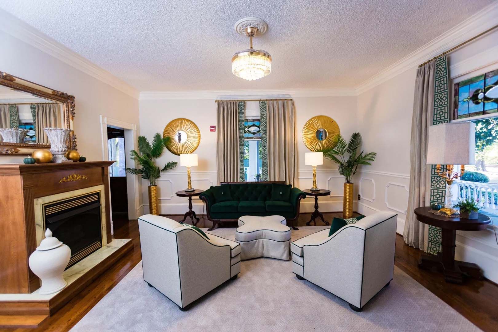 Elegant living room with green velvet sofa, white chairs, gold accents, and fireplace.