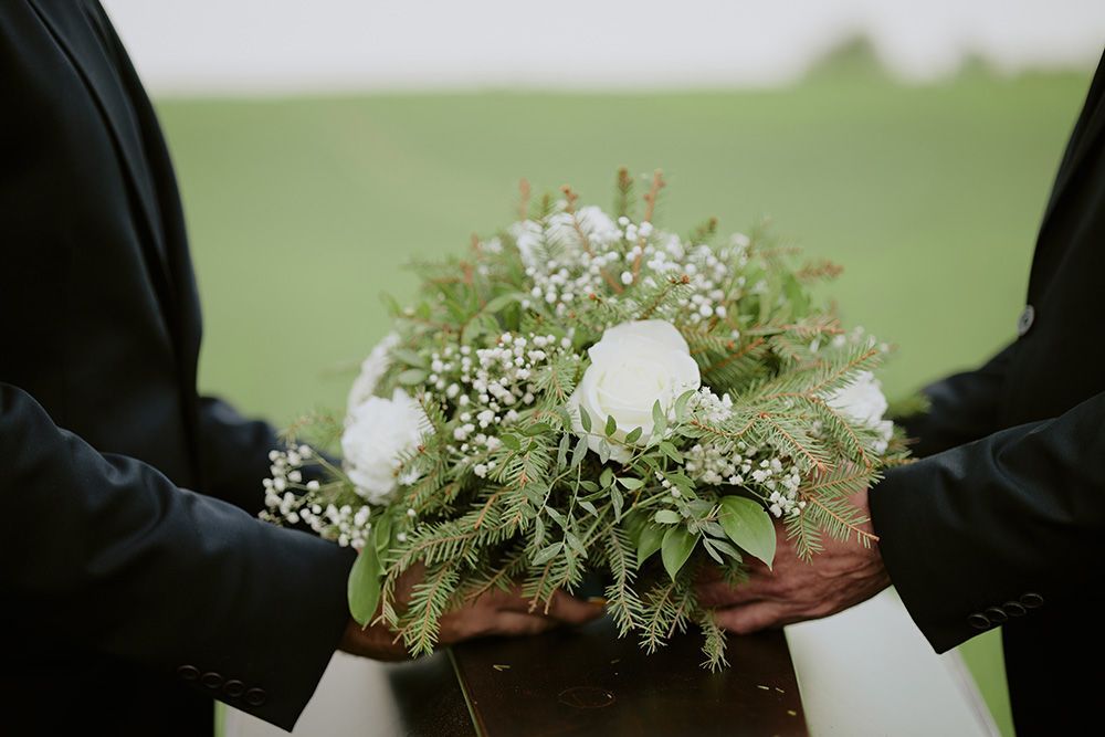 Two people in black suits holding a bouquet of white roses and greenery, outdoors.