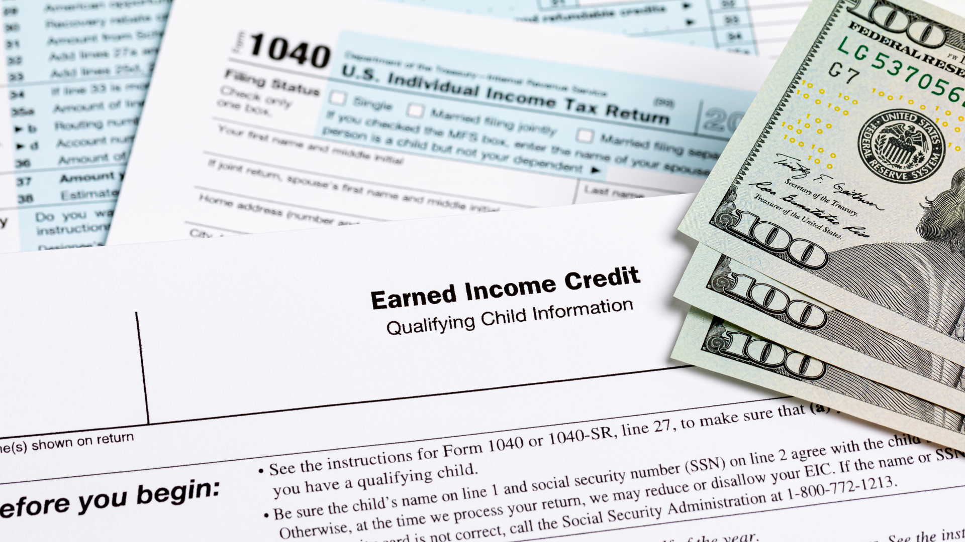 Tax forms, including a 1040, and cash ($100 bills) on a desk.
