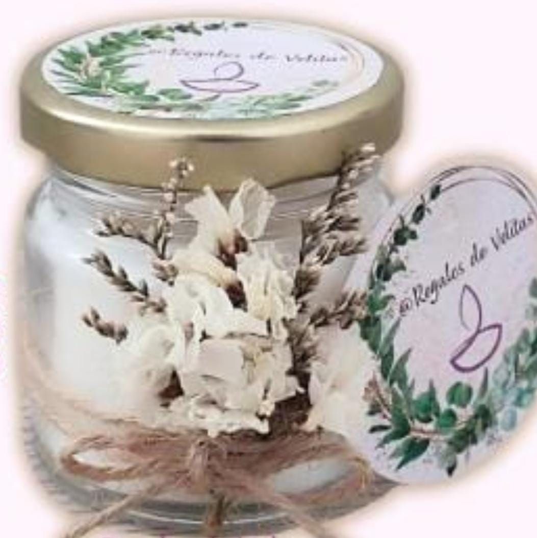 Una vela en frasco con flores secas, cordel y una etiqueta que dice “Regalos de Velitas”.