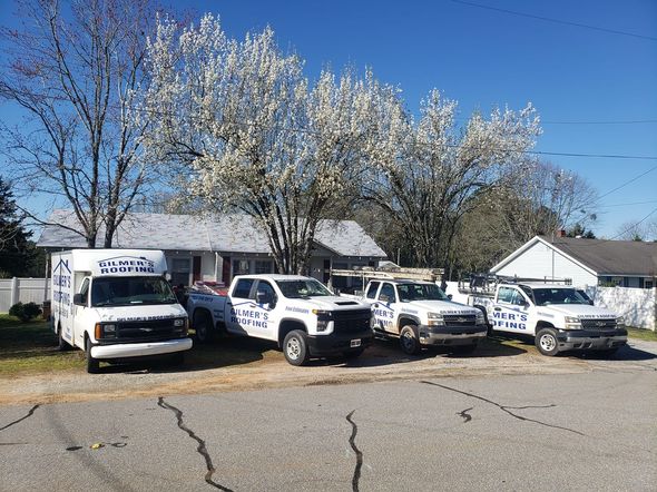 Several white service vehicles parked in front of a house under a flowering tree on a sunny day.