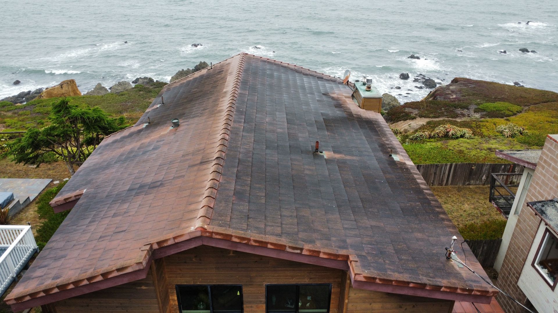 An aerial view of a house with a roof overlooking the ocean.