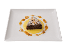 Dessert triangolare al cioccolato, spolverato di zucchero a velo e circondato da salsa all'arancia, servito su un piatto quadrato bianco.