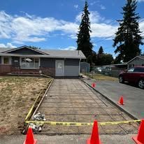 Concrete driveway being poured in front of a house, with safety barriers.