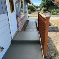 Gray concrete ramp leading up to a blue house with a white door.