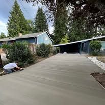 Person smoothing wet concrete driveway near a house.