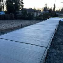 Newly poured concrete sidewalk with wood border, gray with a textured surface, outdoors.
