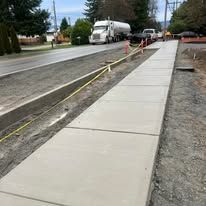 Newly constructed concrete sidewalk next to a road, with a large truck in the background.