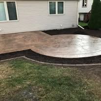 Backyard patio with stamped concrete, near grass and siding of a house.