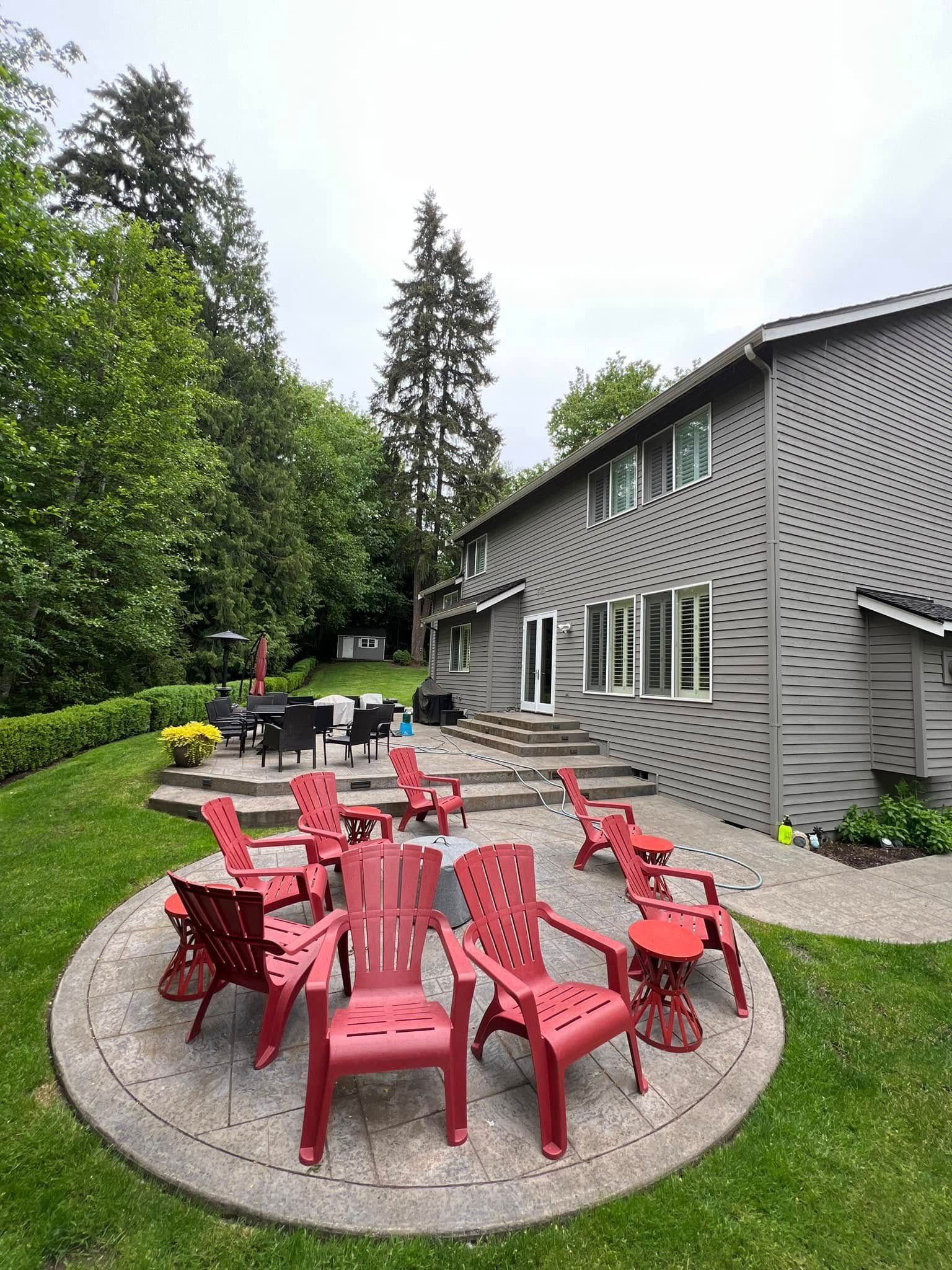 Red chairs on a concrete patio outside a two-story gray house surrounded by greenery.