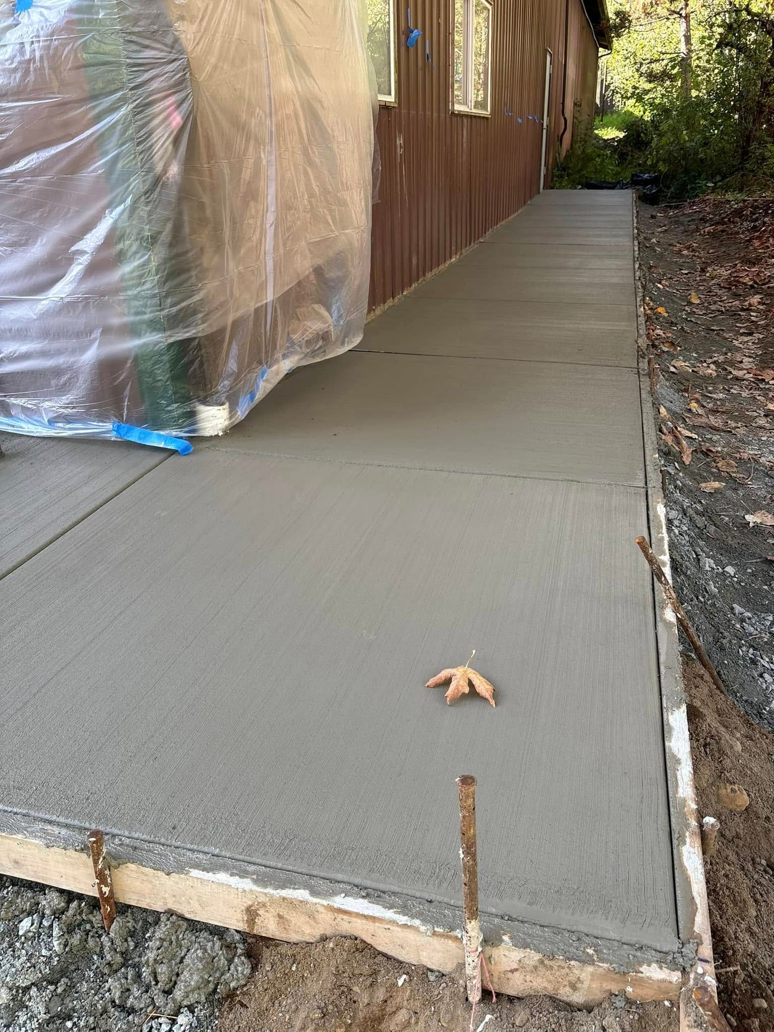 Freshly poured concrete sidewalk next to a brown building, a leaf is on the sidewalk.