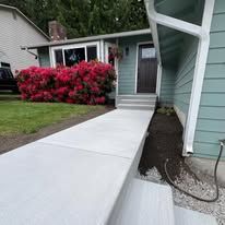 Concrete ramp leading to a house with a door, flanked by bushes and flower bed.