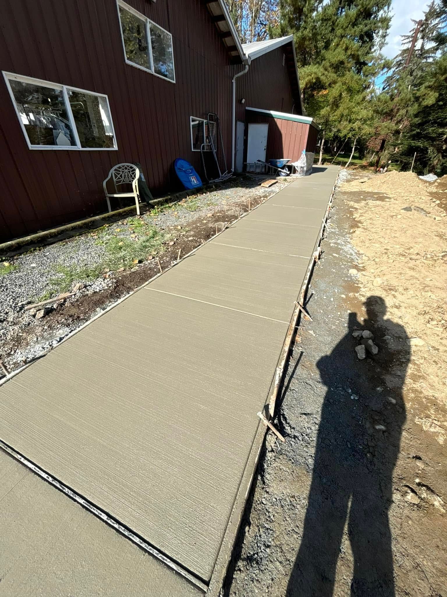 Newly poured concrete walkway next to a red building; a shadow of a person taking the picture is visible.