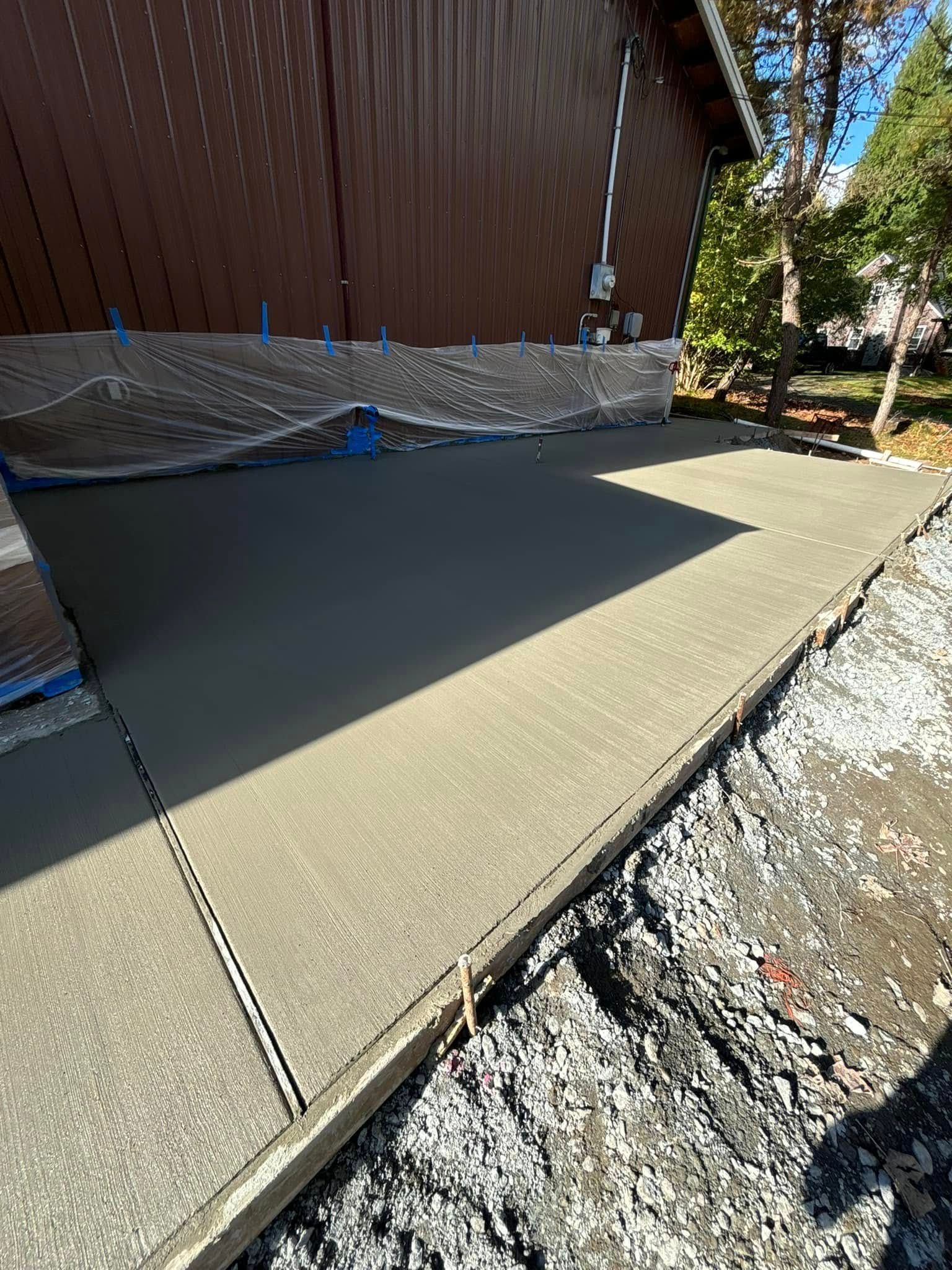 Freshly poured concrete patio next to a brown building. Gravel edge on one side.