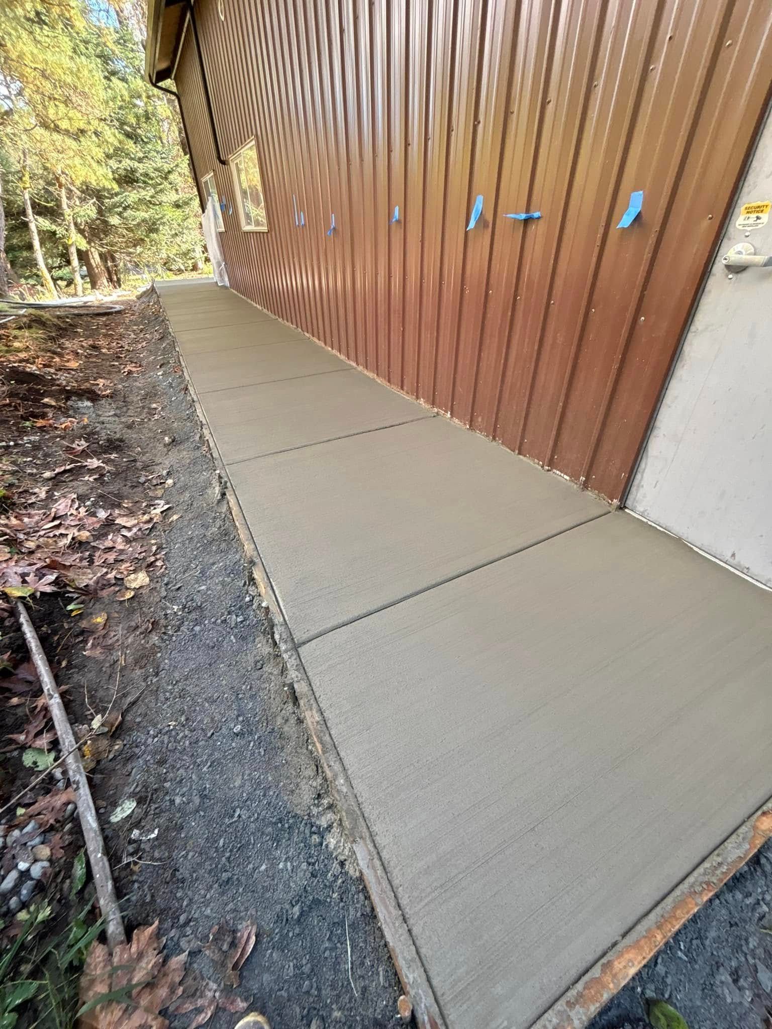 Concrete walkway alongside a brown building with a gravel border and trees.