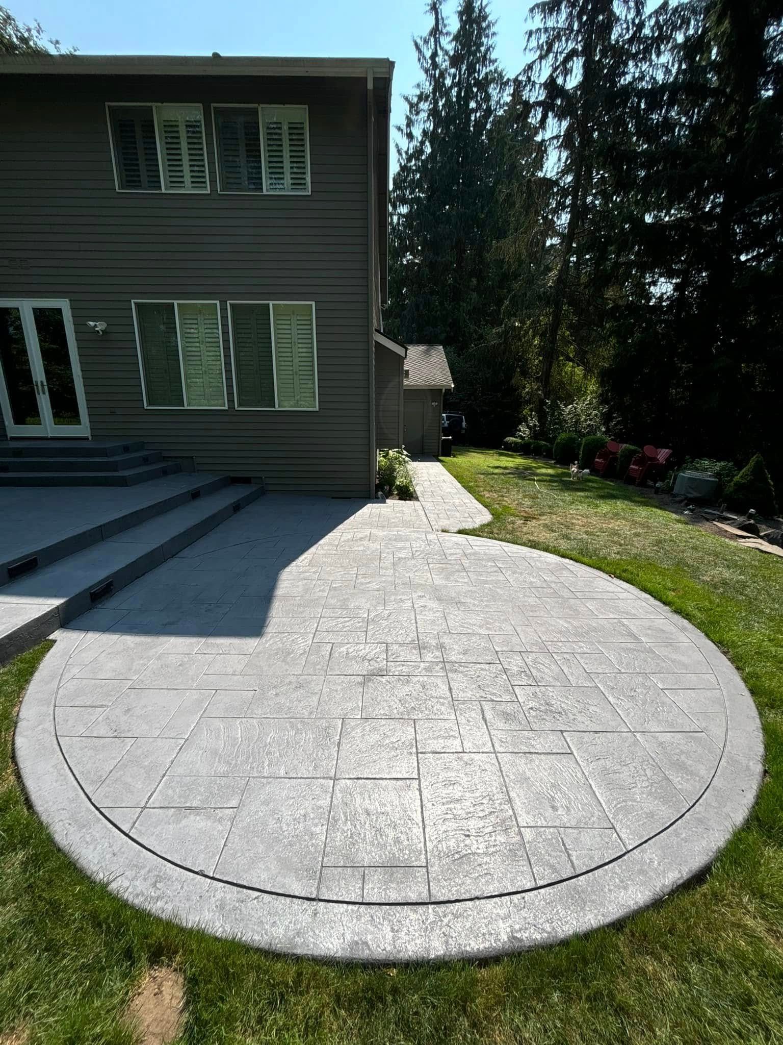 Gray stamped concrete patio with curved border adjacent to a house.