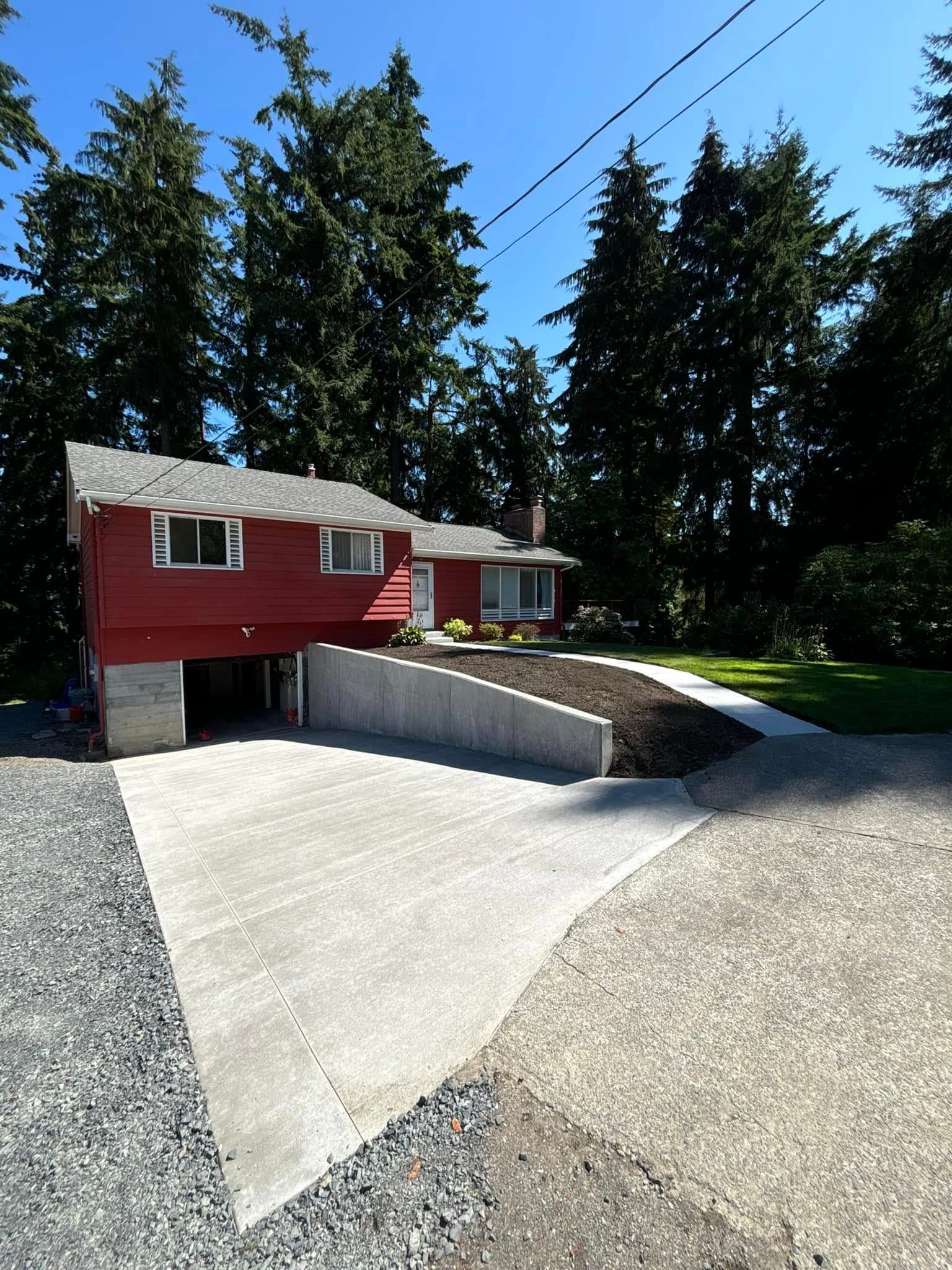 Red house with concrete driveway, surrounded by trees and gravel.