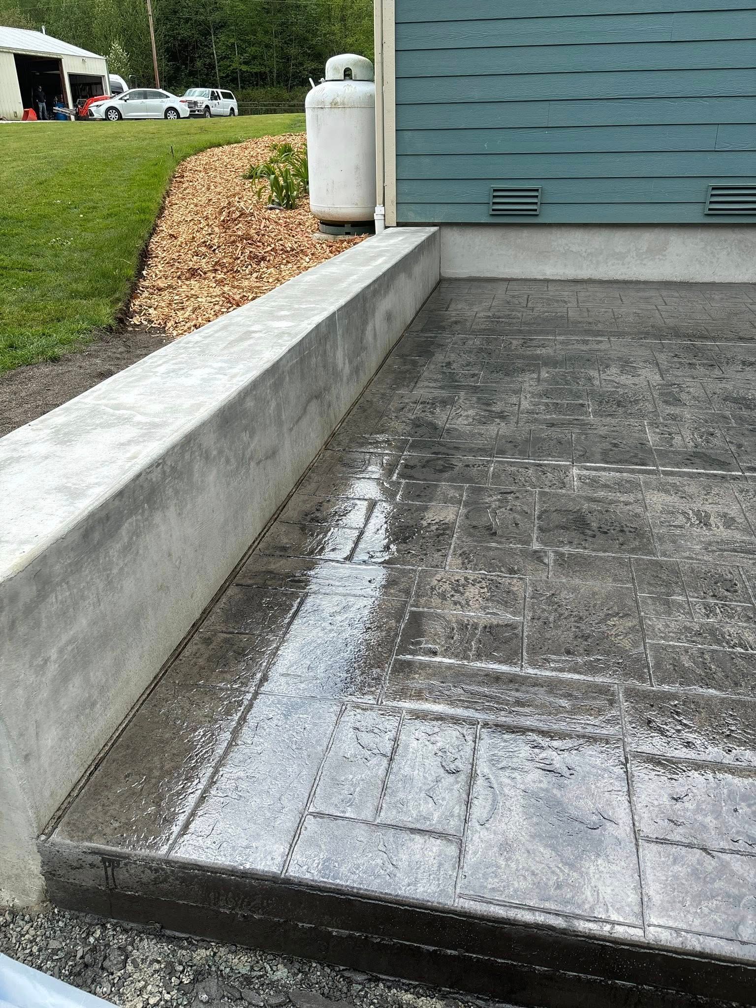 Concrete patio with a retaining wall and a blue-green building in the background.