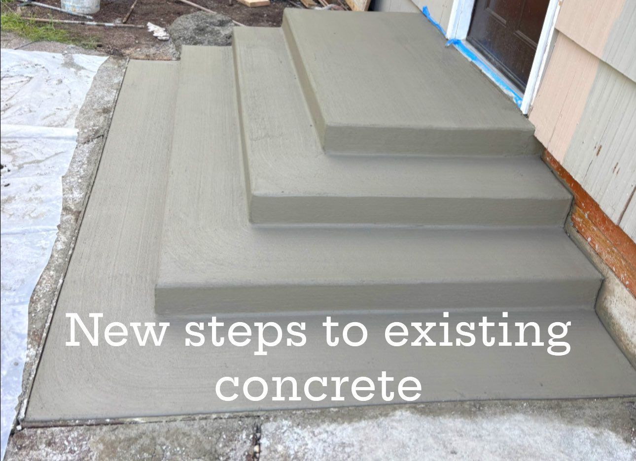 New concrete steps leading to a doorway. Steps are gray; house has wood siding.