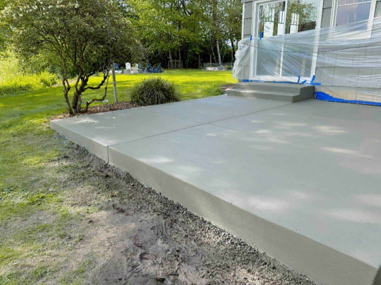 Freshly poured concrete patio with a small step near a house, next to a grassy lawn.