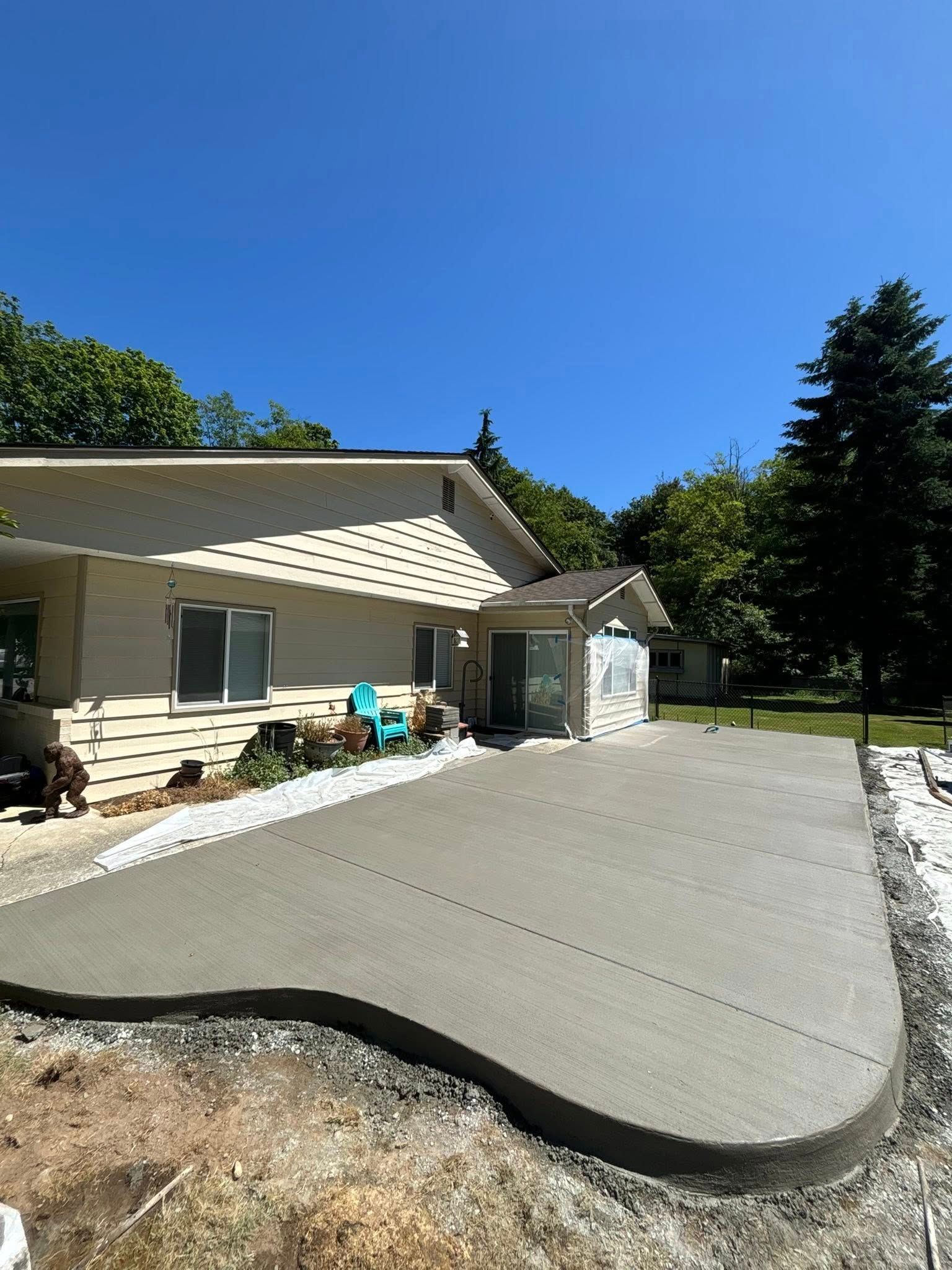 Newly poured concrete patio next to a light-colored house under a blue sky.