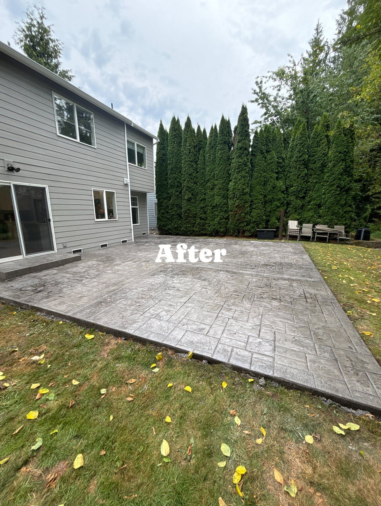 Backyard patio after work, gray pavers, green lawn, house with gray siding, evergreen trees.