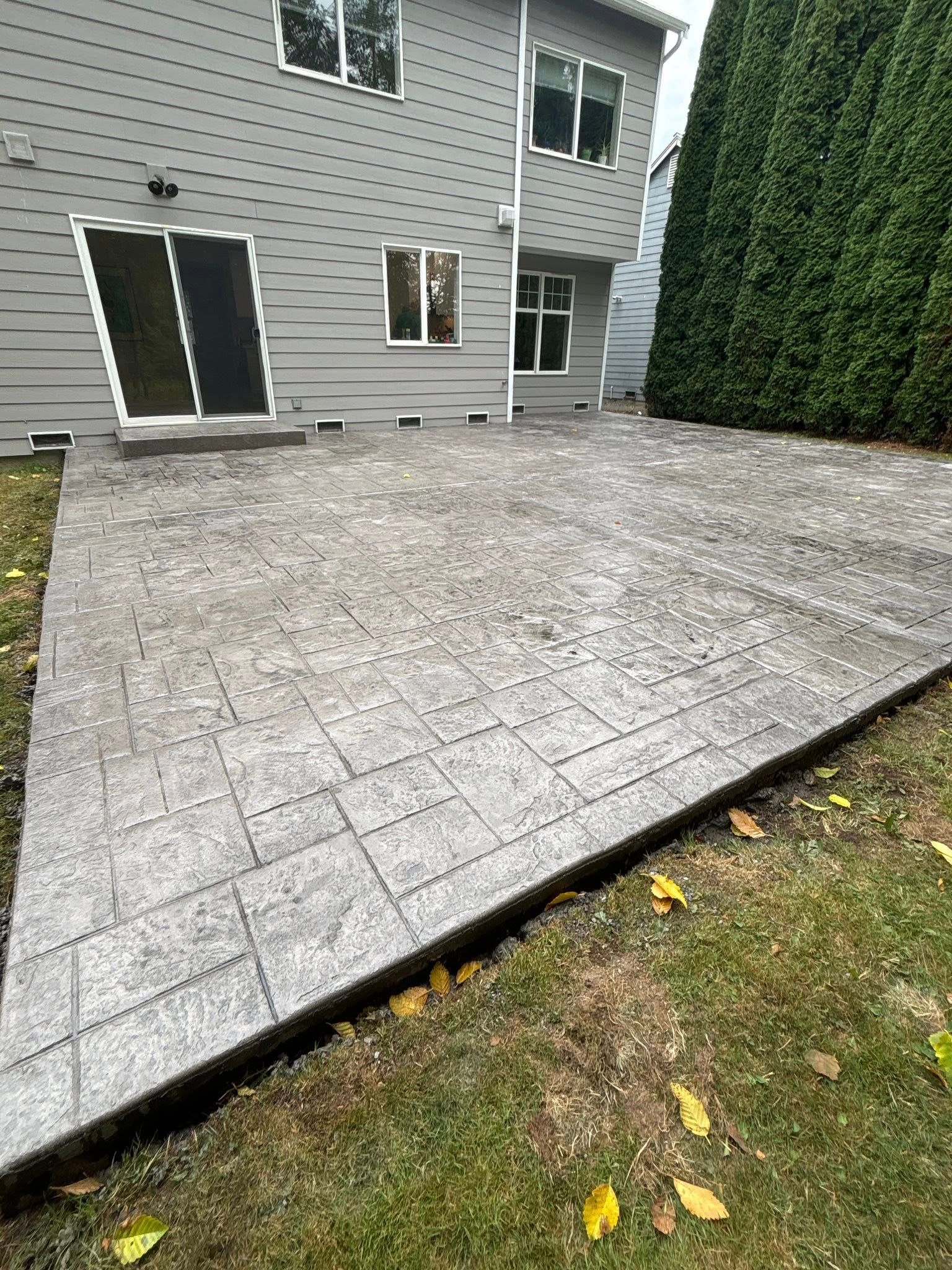 Gray stamped concrete patio next to a house with a sliding glass door and windows.
