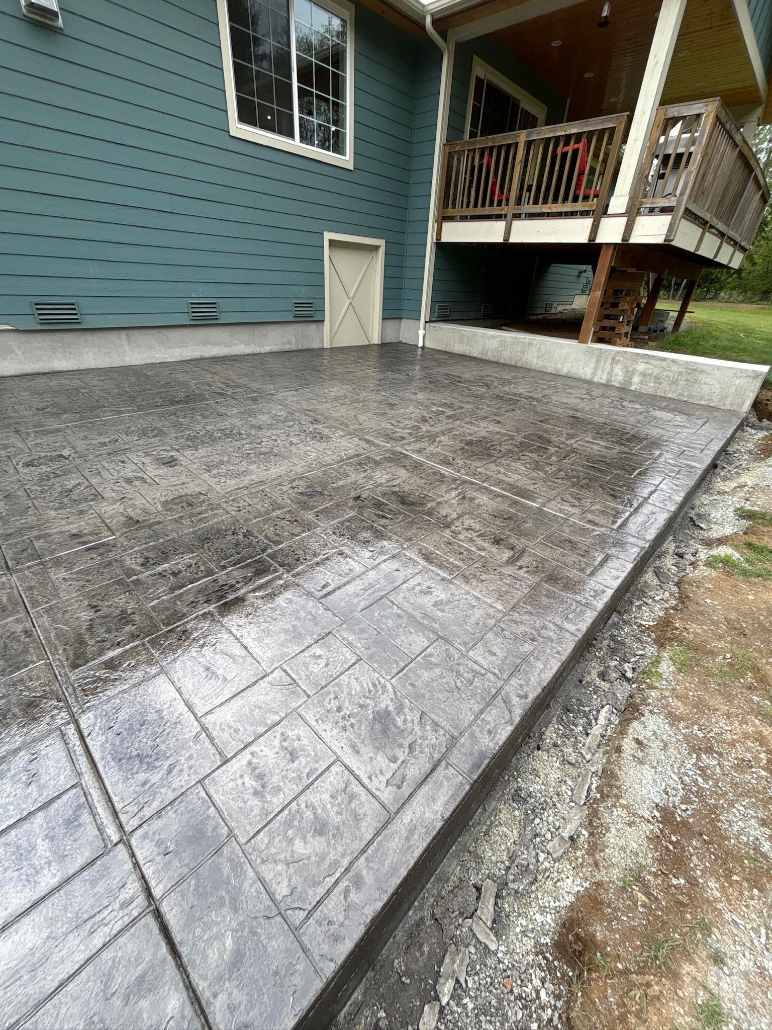 Stamped concrete patio, dark gray, next to blue house with porch.