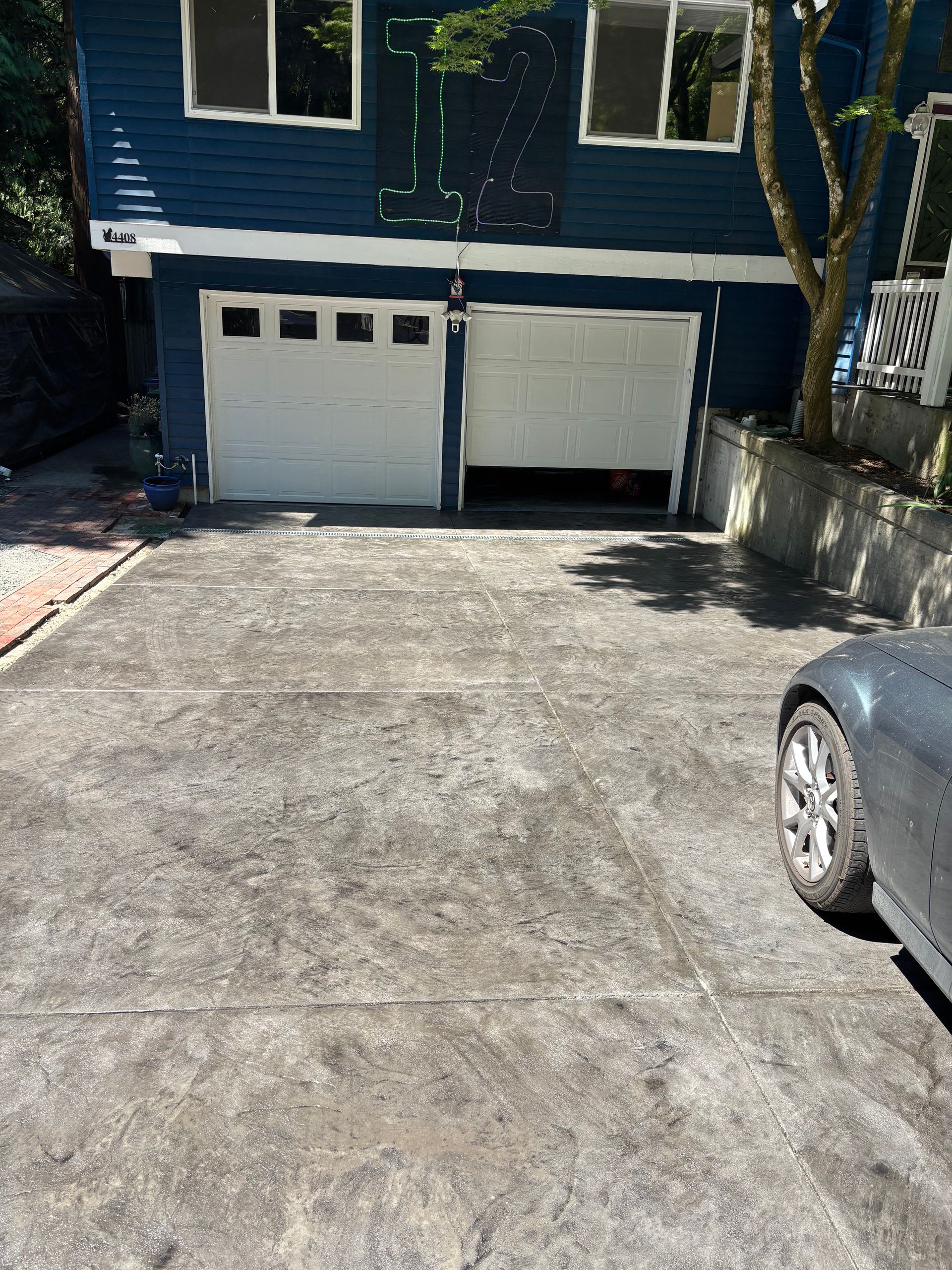 Blue house with two garage doors; one open. Gray car parked on driveway to the right.
