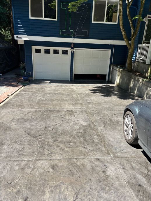 Blue house with two white garage doors; one open. Gray driveway, partially visible car on the right.