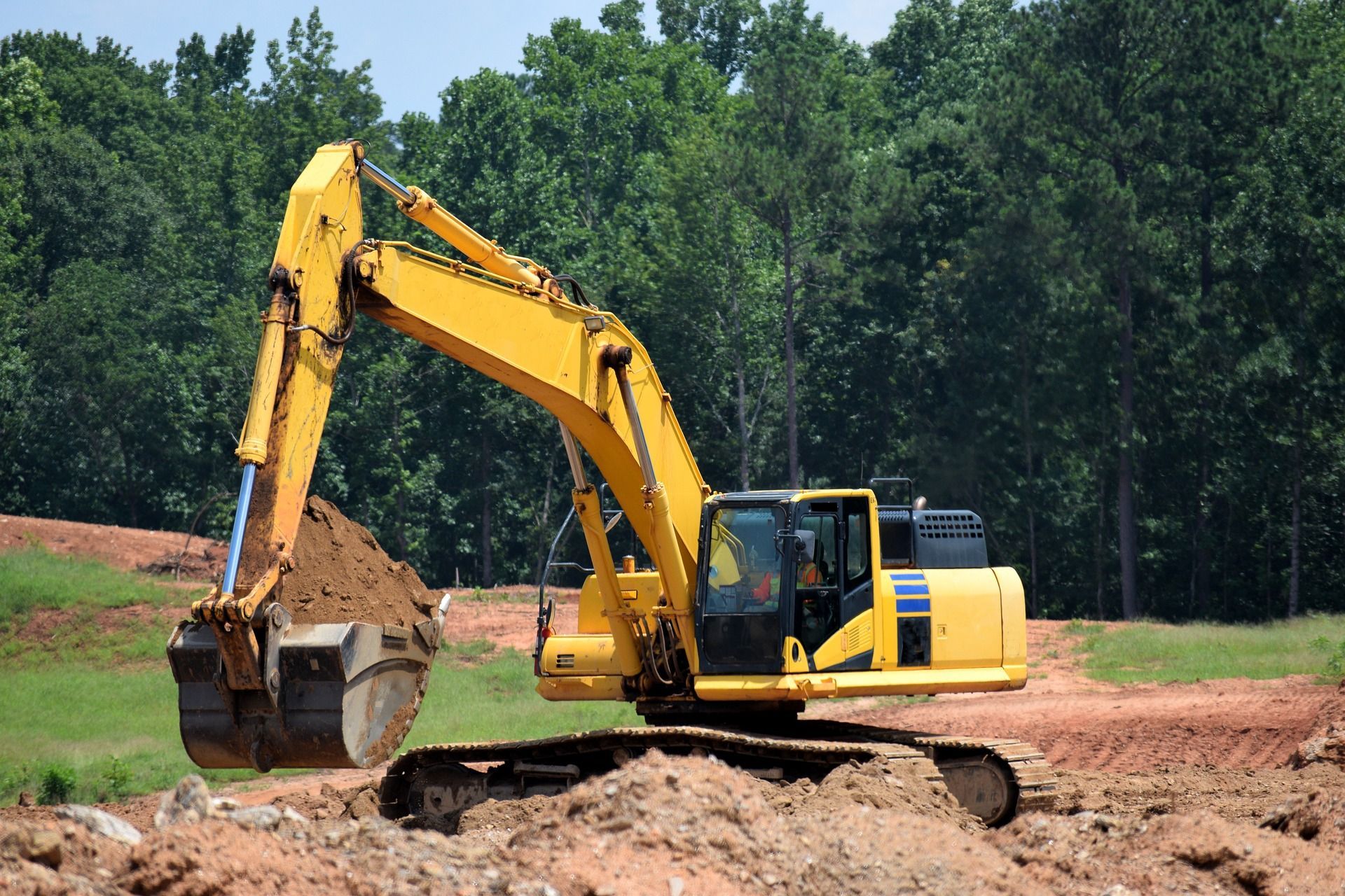 Yellow excavator digging earth at a construction site, with green trees in the background.