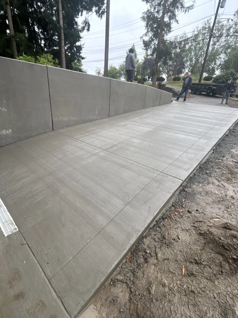 A newly poured concrete ramp leading up to a concrete wall. Workers stand at the top and side of the ramp.