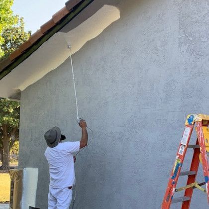 A man is painting the side of a house with a roller.