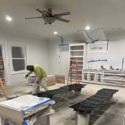 A man is painting a room with a ceiling fan.