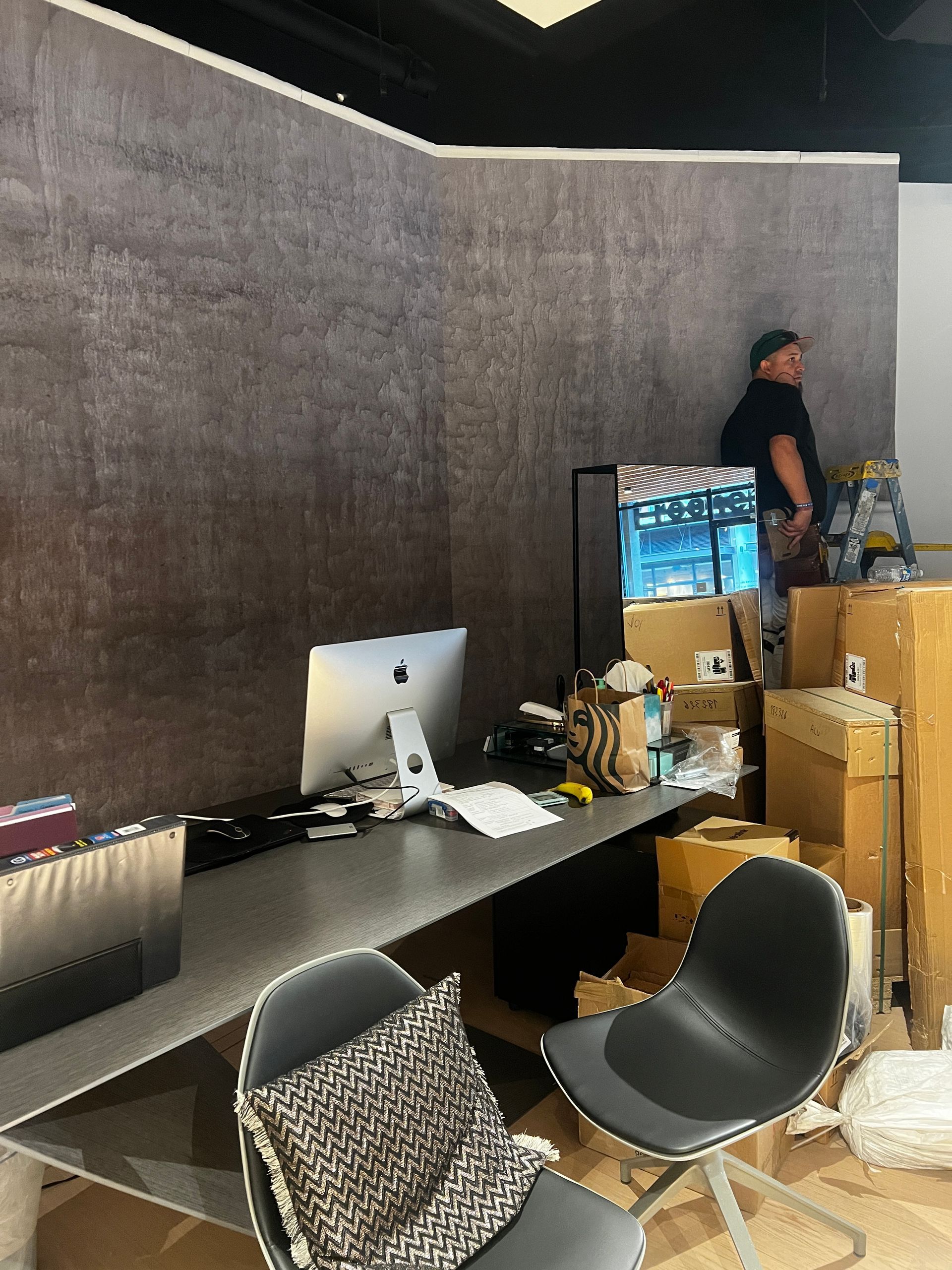 A man is standing in a room with boxes and a desk with a computer on it.