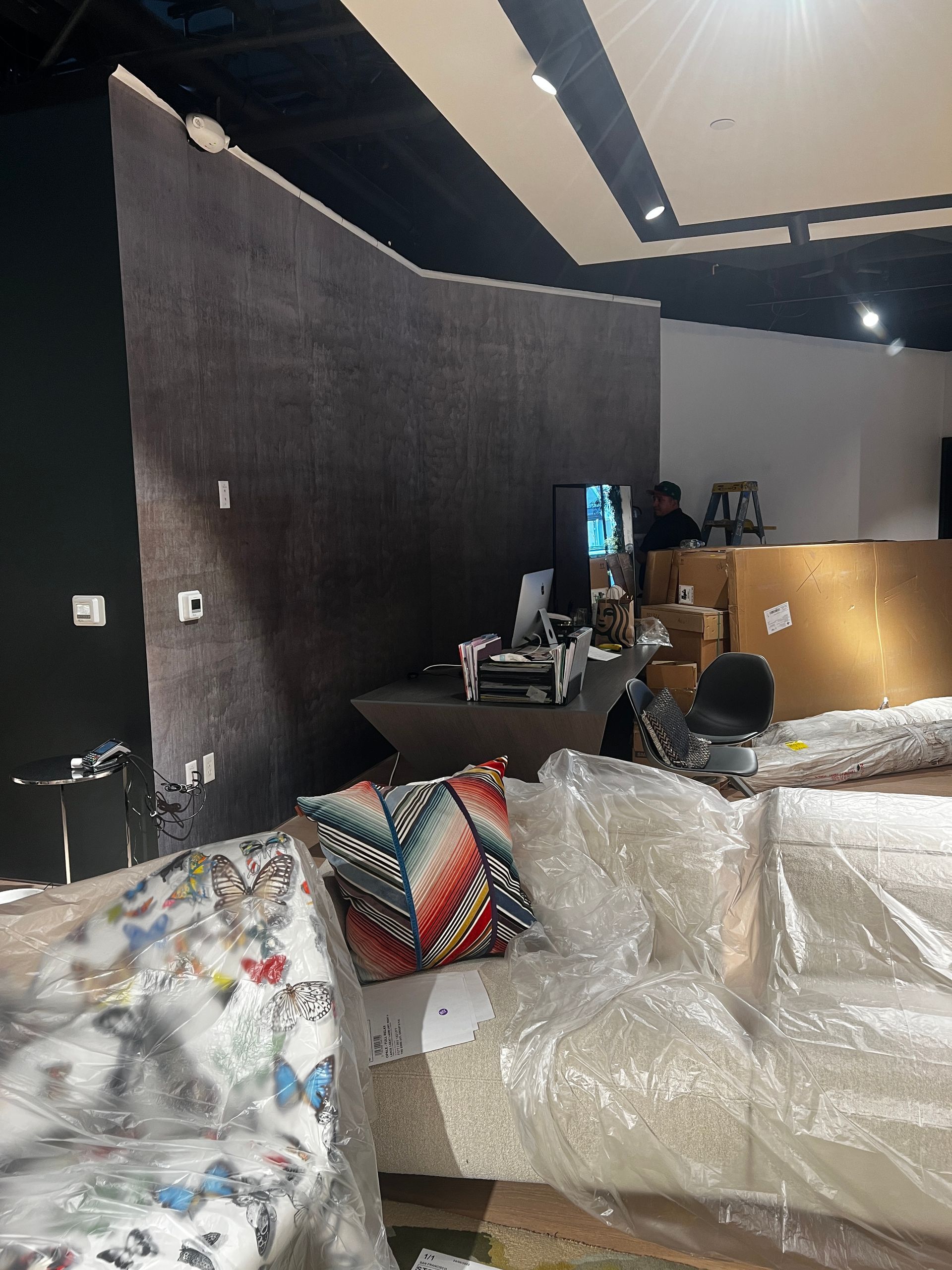 A couch is wrapped in plastic in a room with boxes on the floor.