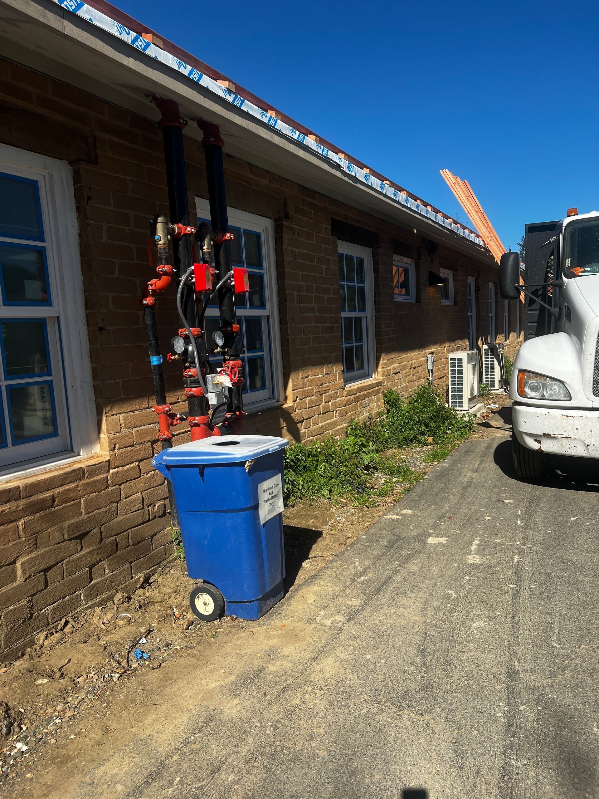 A blue trash can is parked in front of a brick building.