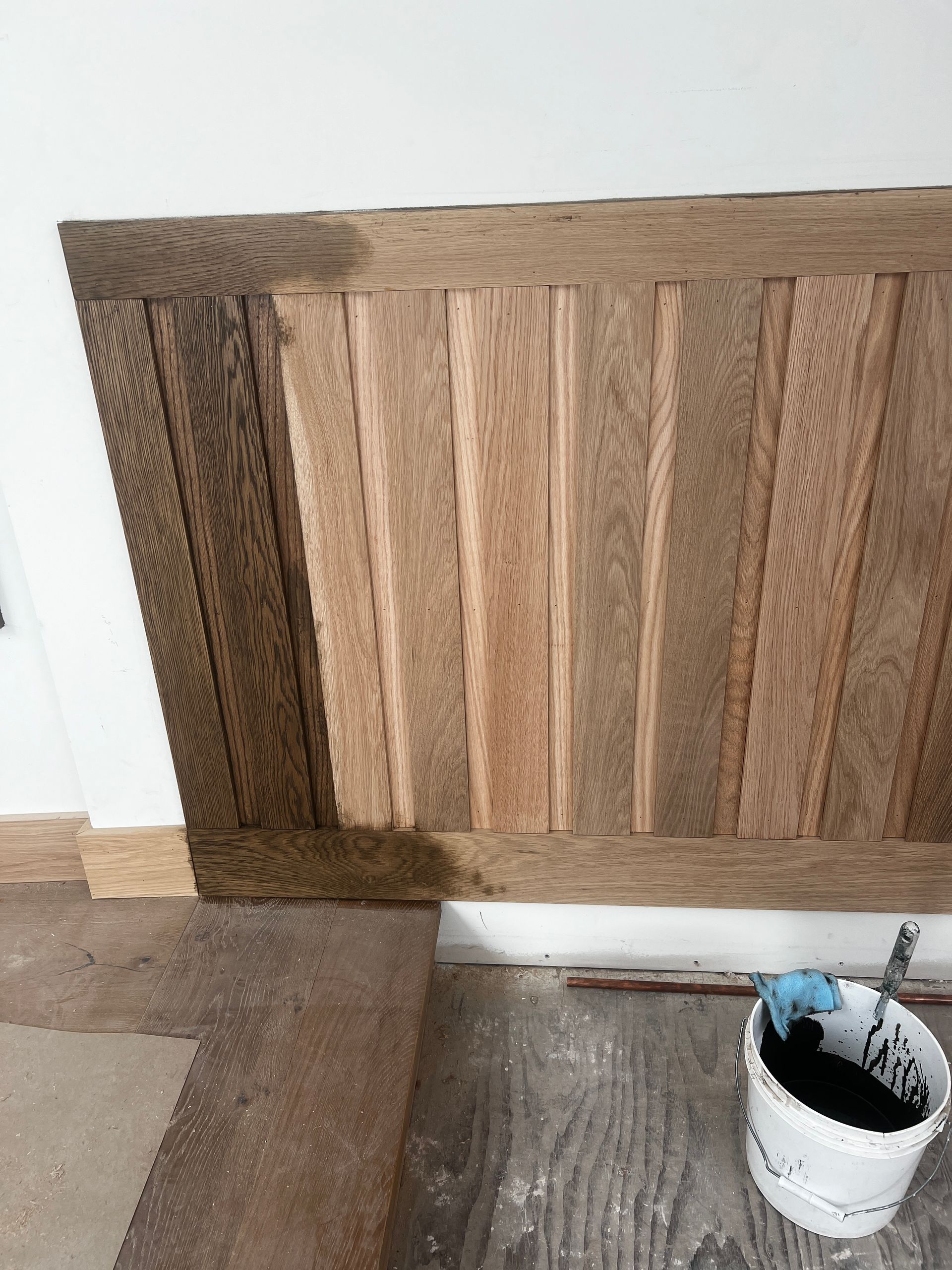 A piece of wood is sitting on a table next to a bucket of paint.