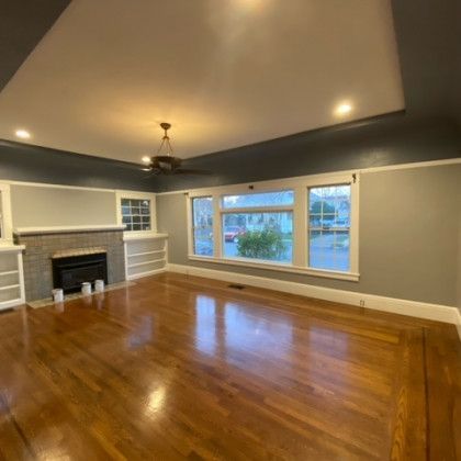 A living room with hardwood floors , a fireplace , and a ceiling fan.