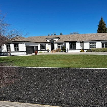 A large white house with a brown roof and a large lawn in front of it