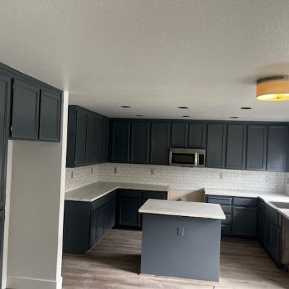 A kitchen with gray cabinets , white counter tops , and a microwave.