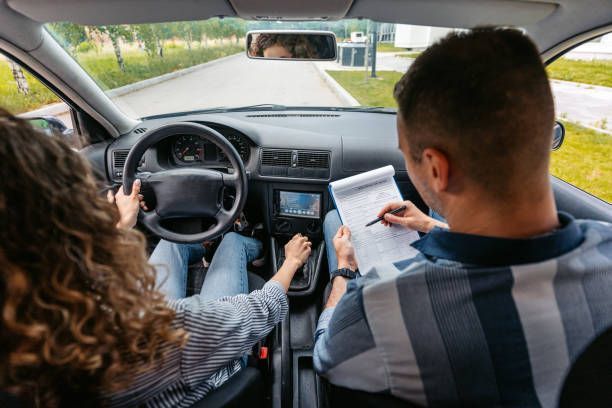 A manual driving test is underway as a focused student is graded by a calm instructor.